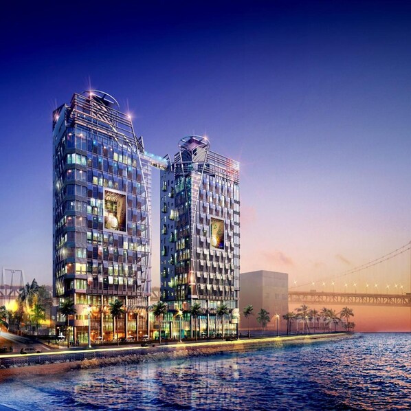 Un hôtel moderne composé de deux immeubles de grande hauteur, offrant une vue sur le front de mer et avec un pont en arrière-plan.