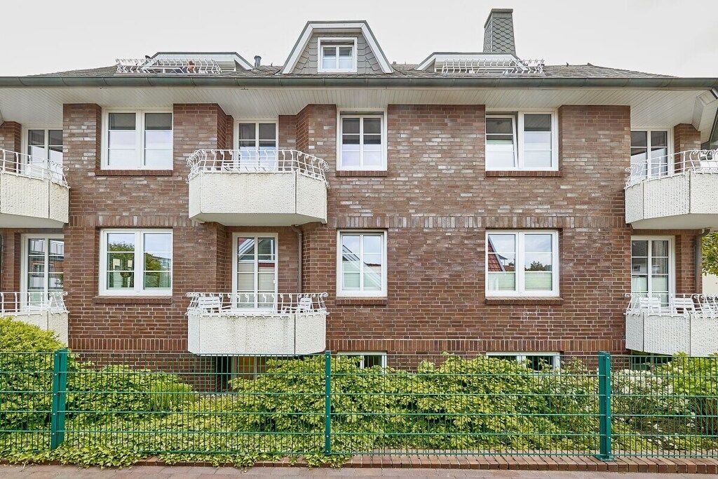 A multi-story brick building with balconies, a green fence, and a brick pathway.