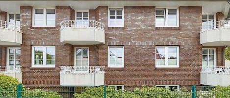 Un edificio de ladrillo de varios pisos con balcones, una cerca verde y un camino de ladrillo.