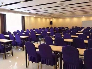 A conference room with rows of tables and chairs, a projector screen, and a speaker.