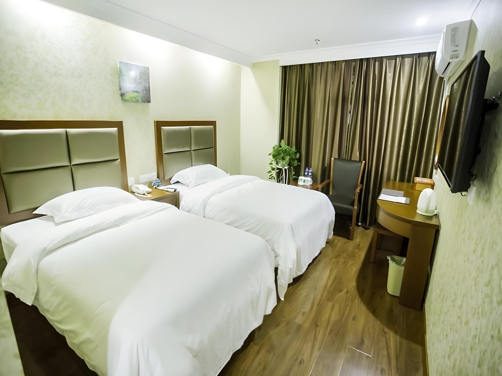 A hotel room with two beds, a desk, a chair, a mirror, a plant, and a TV mounted on the wall.