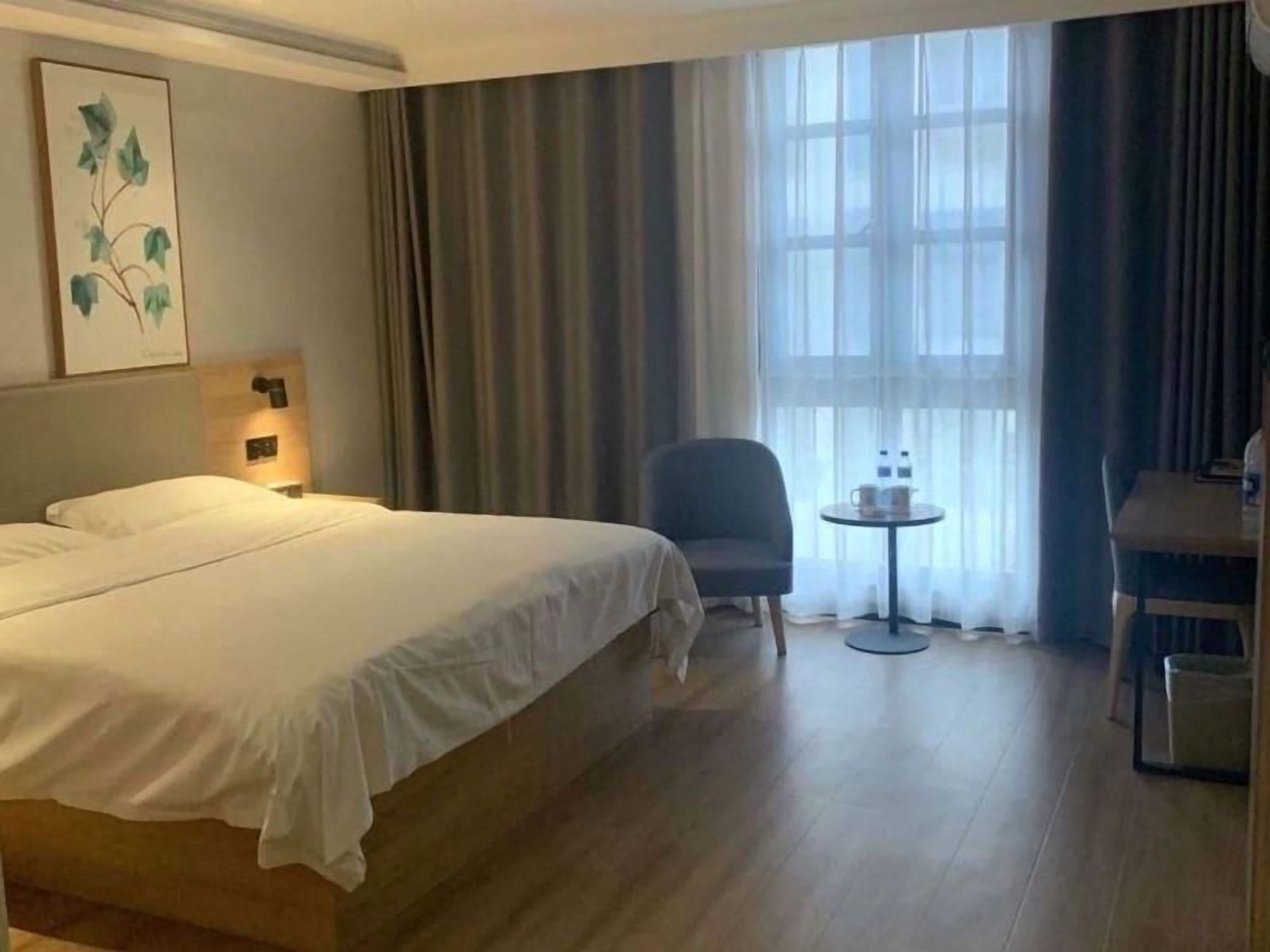 A hotel room with a bed, two chairs, a small table, and a window with curtains.