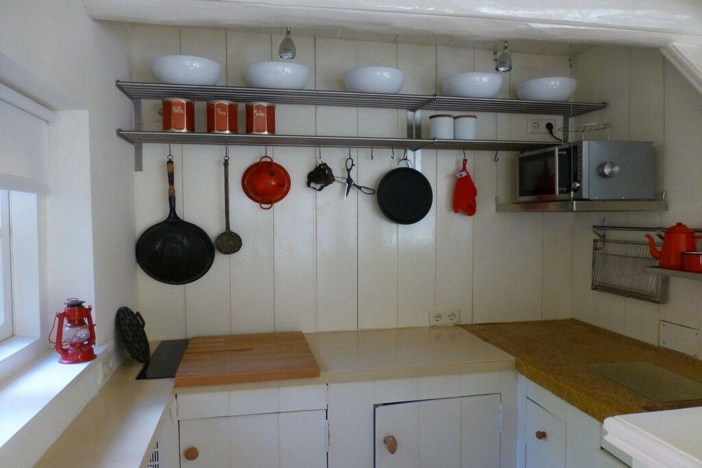 Een keuken met witte kastjes, een houten aanrecht, hangende pannen, een magnetron en planken met kommen en potten.