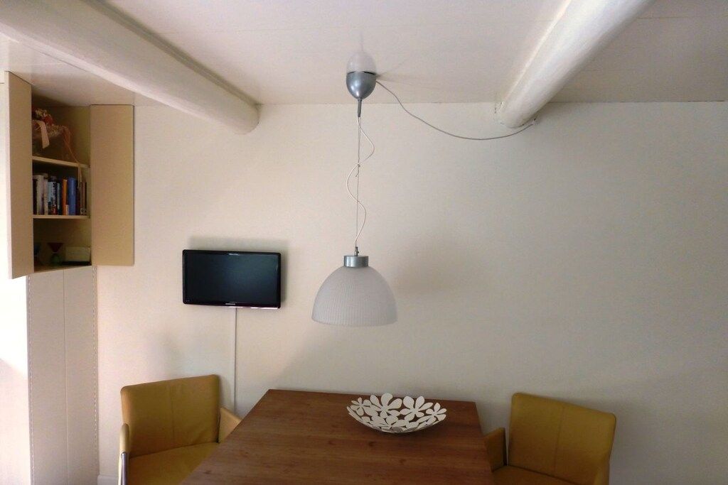 En matplats med ett träbord, två stolar, en vit hänglampa och en platt-TV som är monterad på väggen.