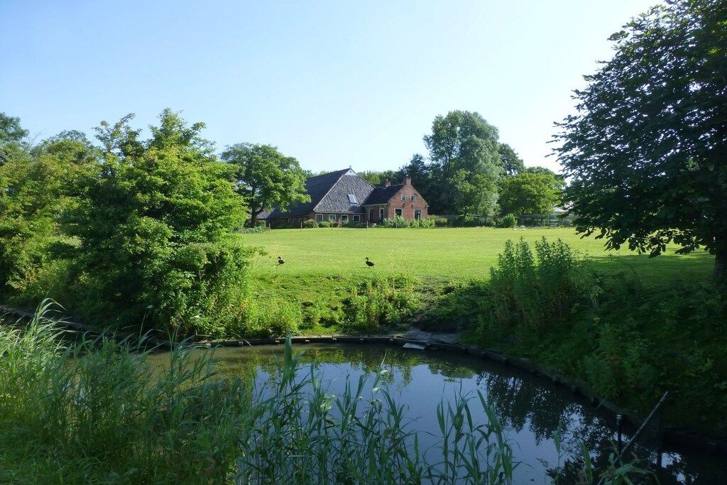A house with a pond in the foreground and a grassy field in the background.
