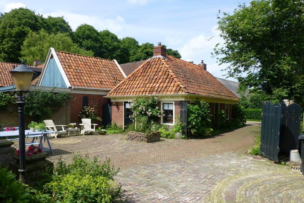 Une cour avec un bâtiment en briques, des sièges en plein air et une structure dotée d’un toit de chaume.