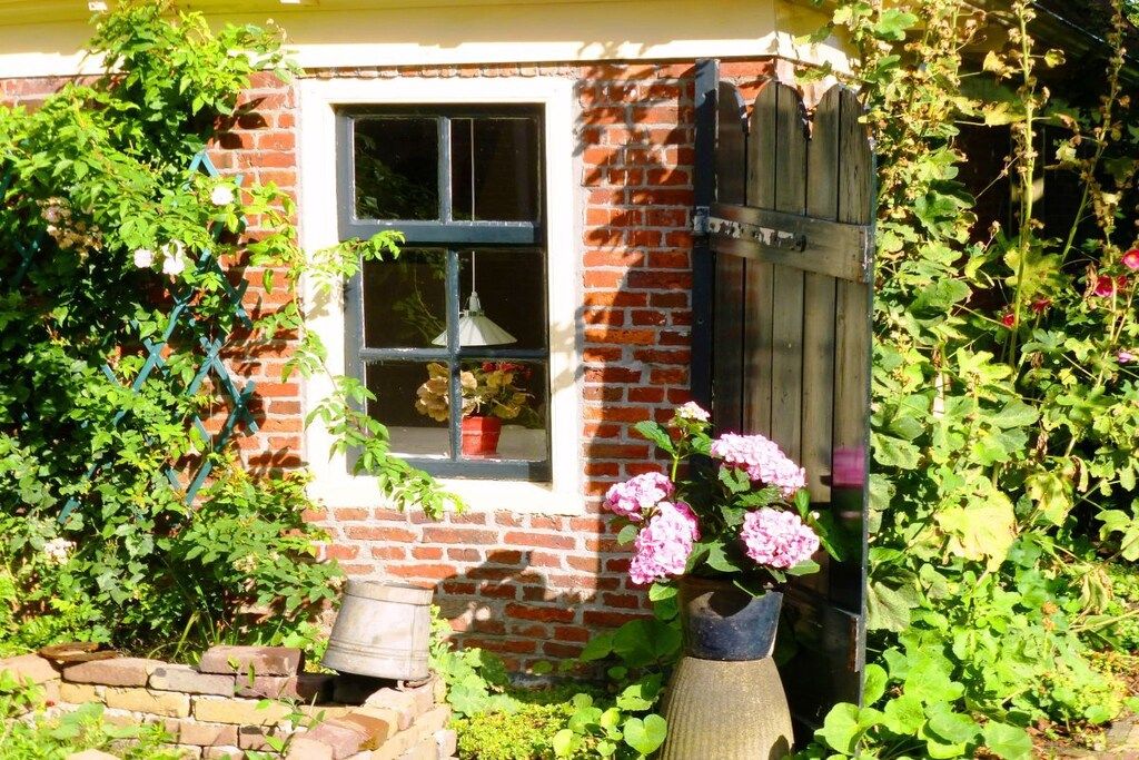 Een gebouw van baksteen met een raam, een deur en planten in potten.