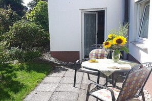 Eine Terrasse im Freien mit Tisch und Stühlen, ein Blumentopf mit Sonnenblumen und ein Gebäude im Hintergrund.