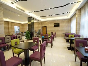 A hotel dining area with multiple tables and chairs, a kitchen in the background, and a large mirror on the wall. - Lavande Hotel (Qingyuan)