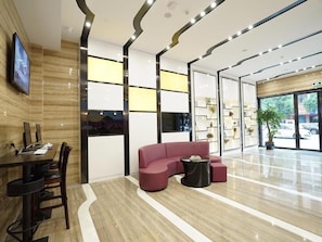 A modern lobby with a curved red sofa, a dining area with a table and chairs, and a large window offering a view of the street. - Lavande Hotel (Qingyuan)