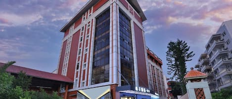 Um hotel com vários andares, uma entrada imponente, área externa coberta e céu claro.