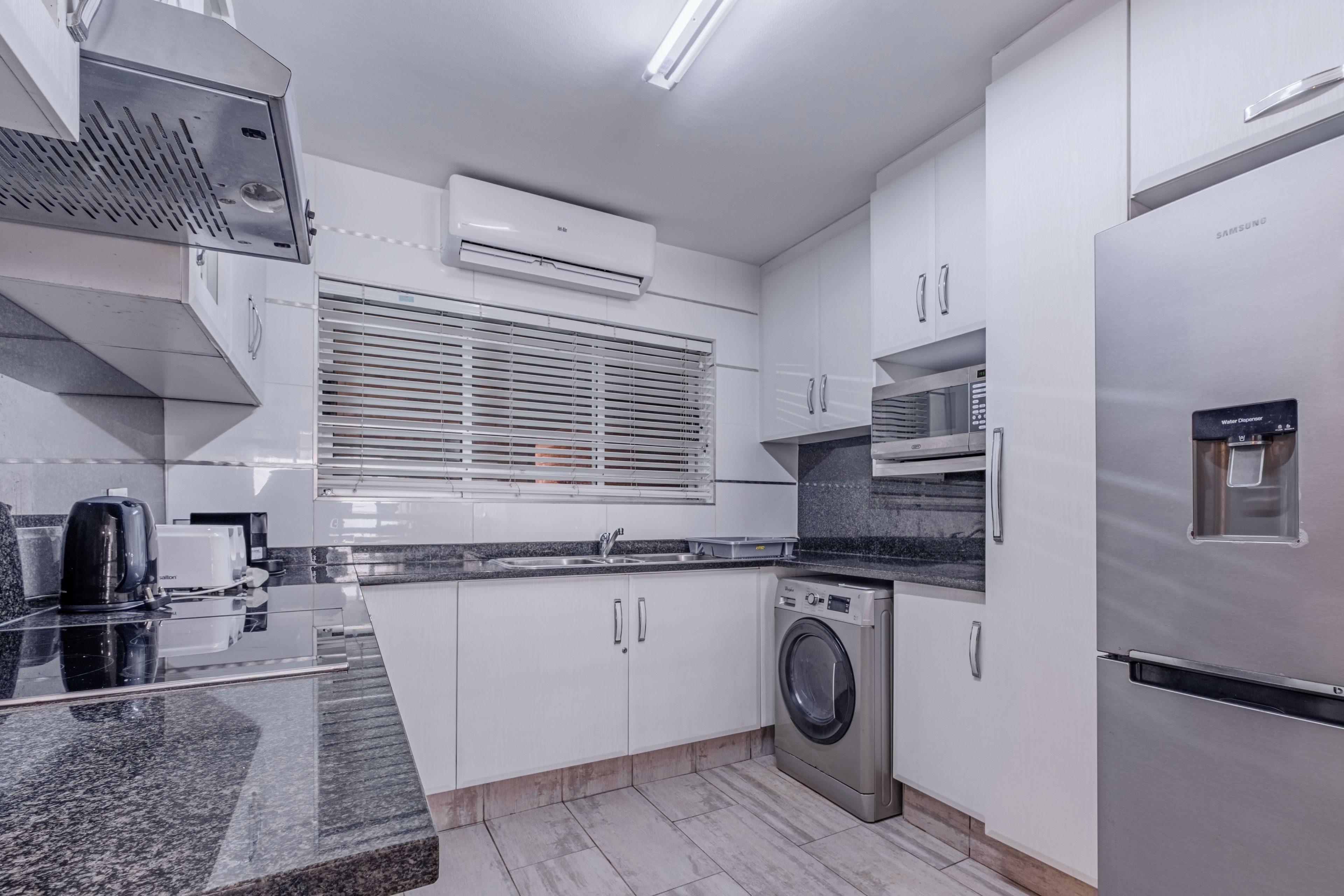 Une cuisine moderne avec des meubles blancs, un four encastré, un lave-linge et un distributeur d’eau.