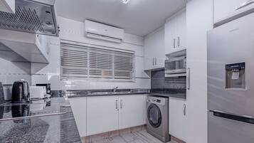 Une cuisine moderne avec des meubles blancs, un four encastré, un lave-linge et un distributeur d’eau.