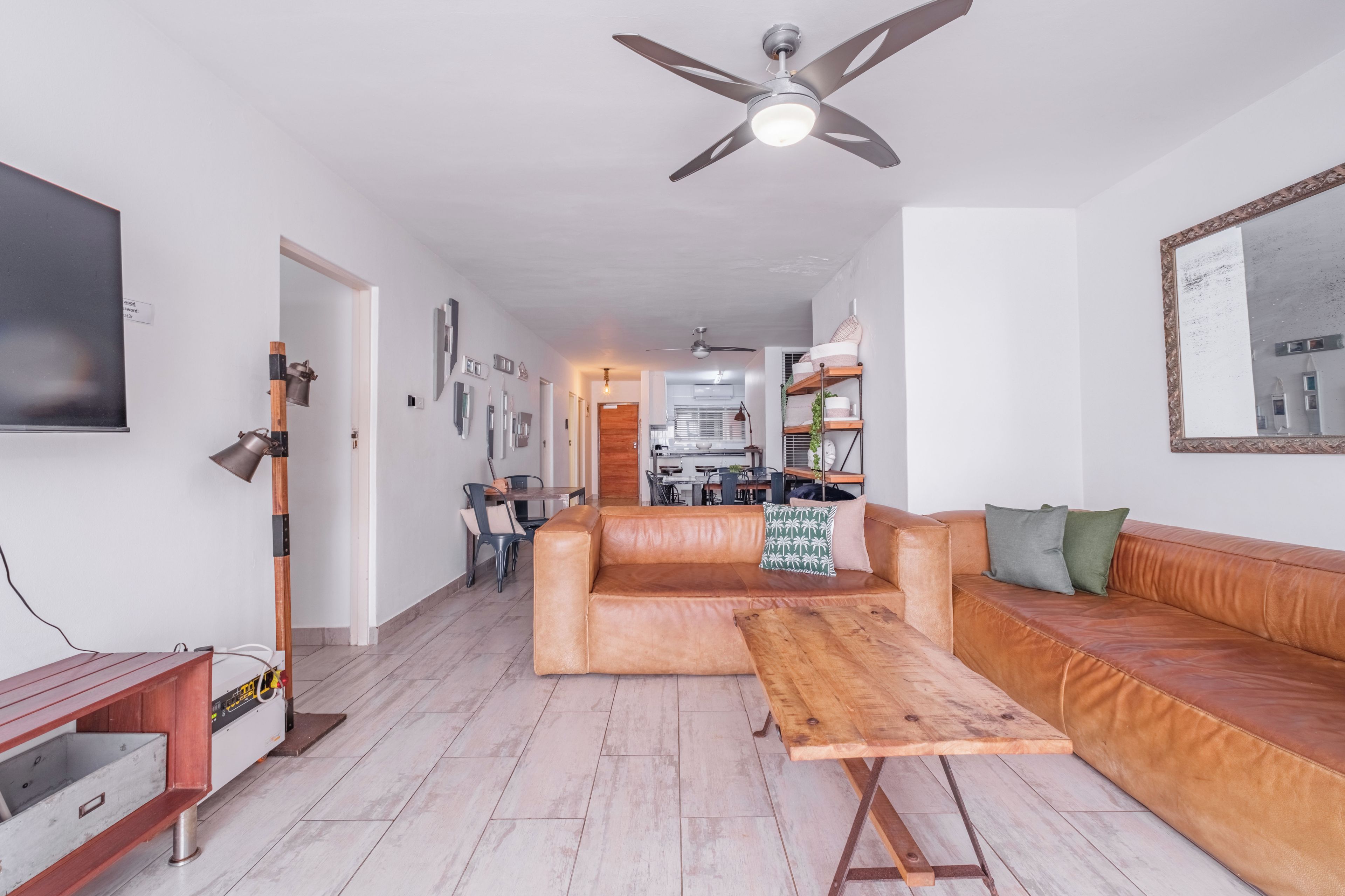 Ein modernes Wohnzimmer mit einer Ledersofa, einem Holztisch und einem Deckenventilator.