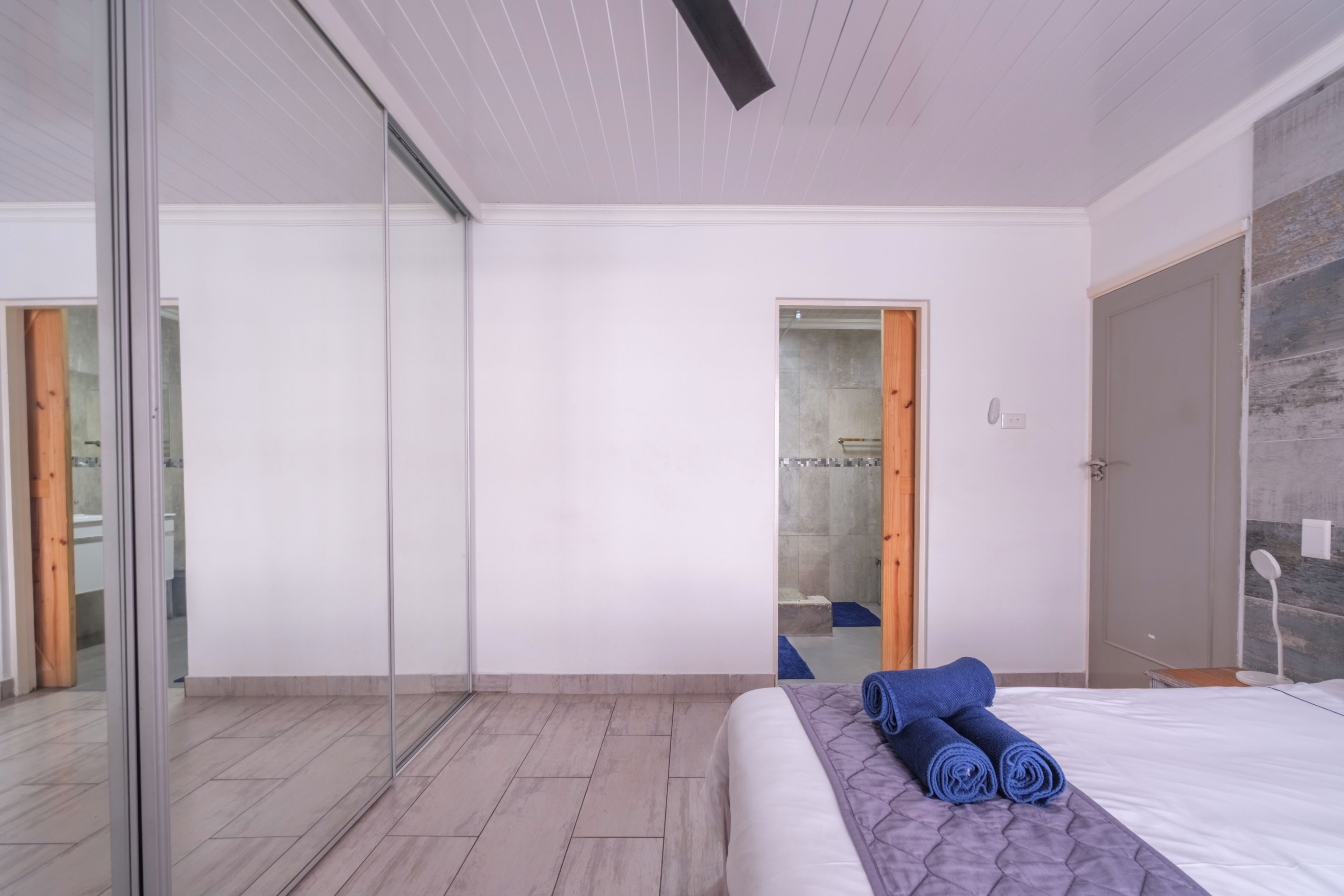 Une chambre à coucher moderne avec un grand lit, une porte en verre donnant sur une salle de bain et une porte en bois menant à une cabine de douche.