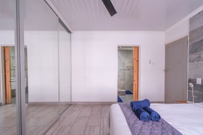 A modern bedroom with a large bed, a glass door leading to a bathroom, and a wooden door to a shower area.