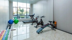 Un gimnasio con equipo de ejercicio, un ventanal con vista a coches estacionados y suelo de baldosas.