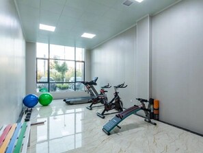 Un gimnàs amb equipament d'exercici, una finestra amb vista a cotxes aparcats i un sòl de rajoles.