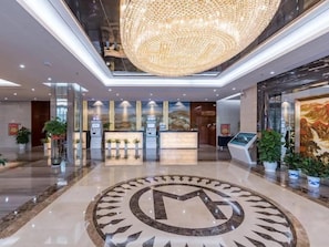 Un vestíbul d'hotel amb una recepció, una gran pèndol i un emblema circular al sòl.