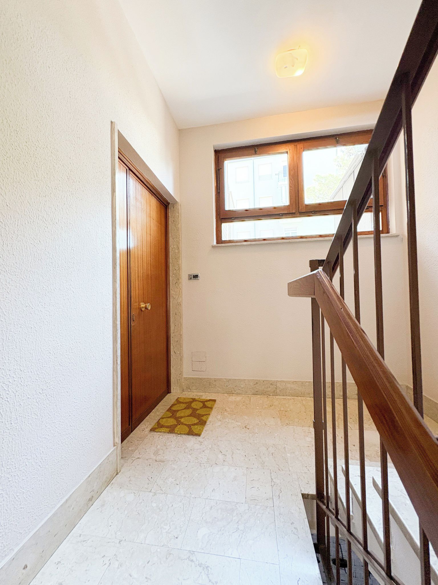 A hallway with a wooden door, a window, and a staircase.
