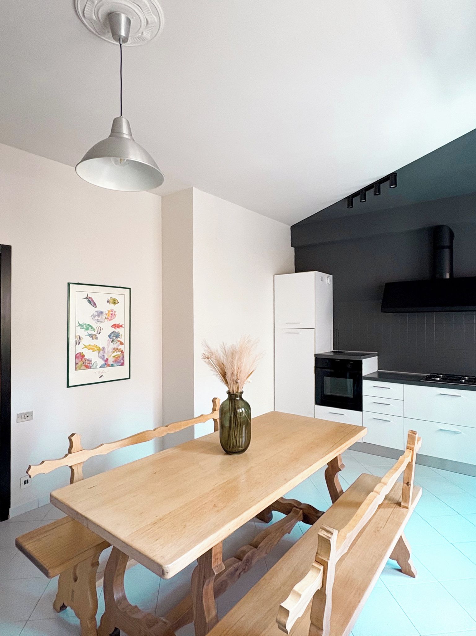 Una cucina moderna con mobili bianchi, un piano cottura nero e un tavolo da pranzo in legno con panche.
