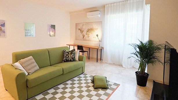 A living room with a green sofa, a checkered rug, a dining table, and a potted plant. - Borgo Design Apartment by the sea (Civitavecchia)