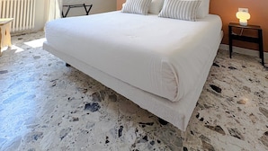 A bedroom with a large bed, a nightstand with a lamp, a window with curtains, and a radiator. - Borgo Design Apartment by the sea (Civitavecchia)
