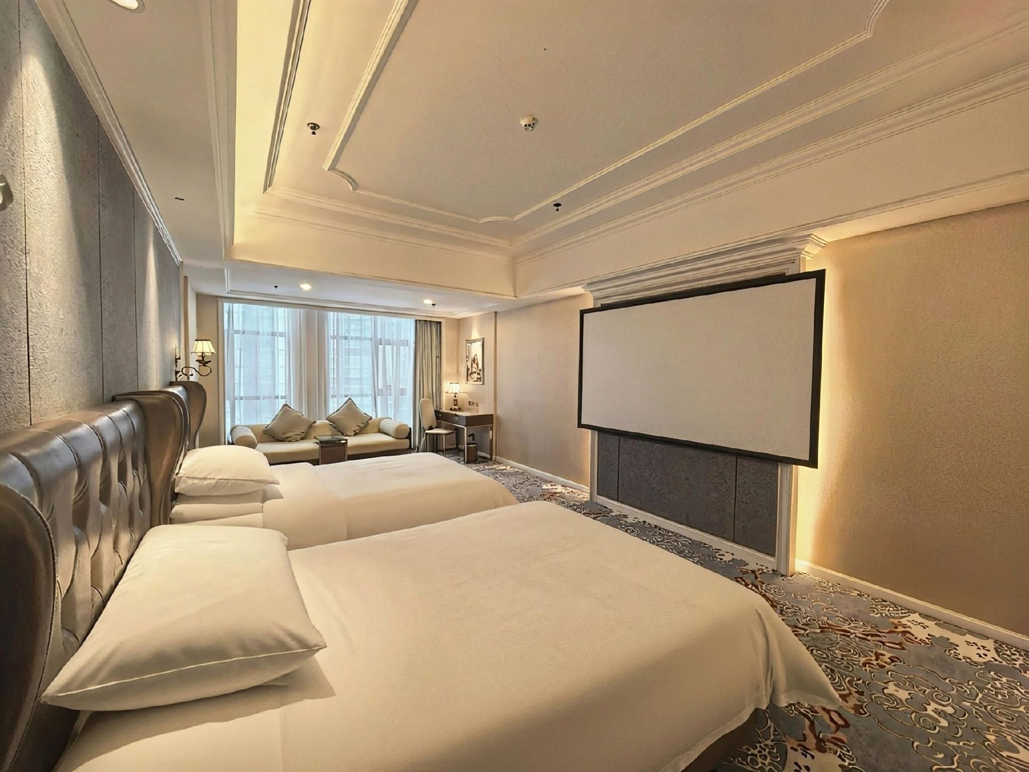 A hotel room with two beds, a desk, a chair, a television, and a large window.