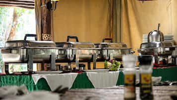 Disposición de bufé con varios recipientes de acero inoxidable, una mesa con mantel verde y una lámpara colgante de mimbre.