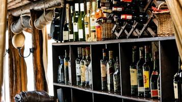 A bar area with shelves stocked with various bottles of alcohol, a leather chair, and a rustic wooden ceiling.