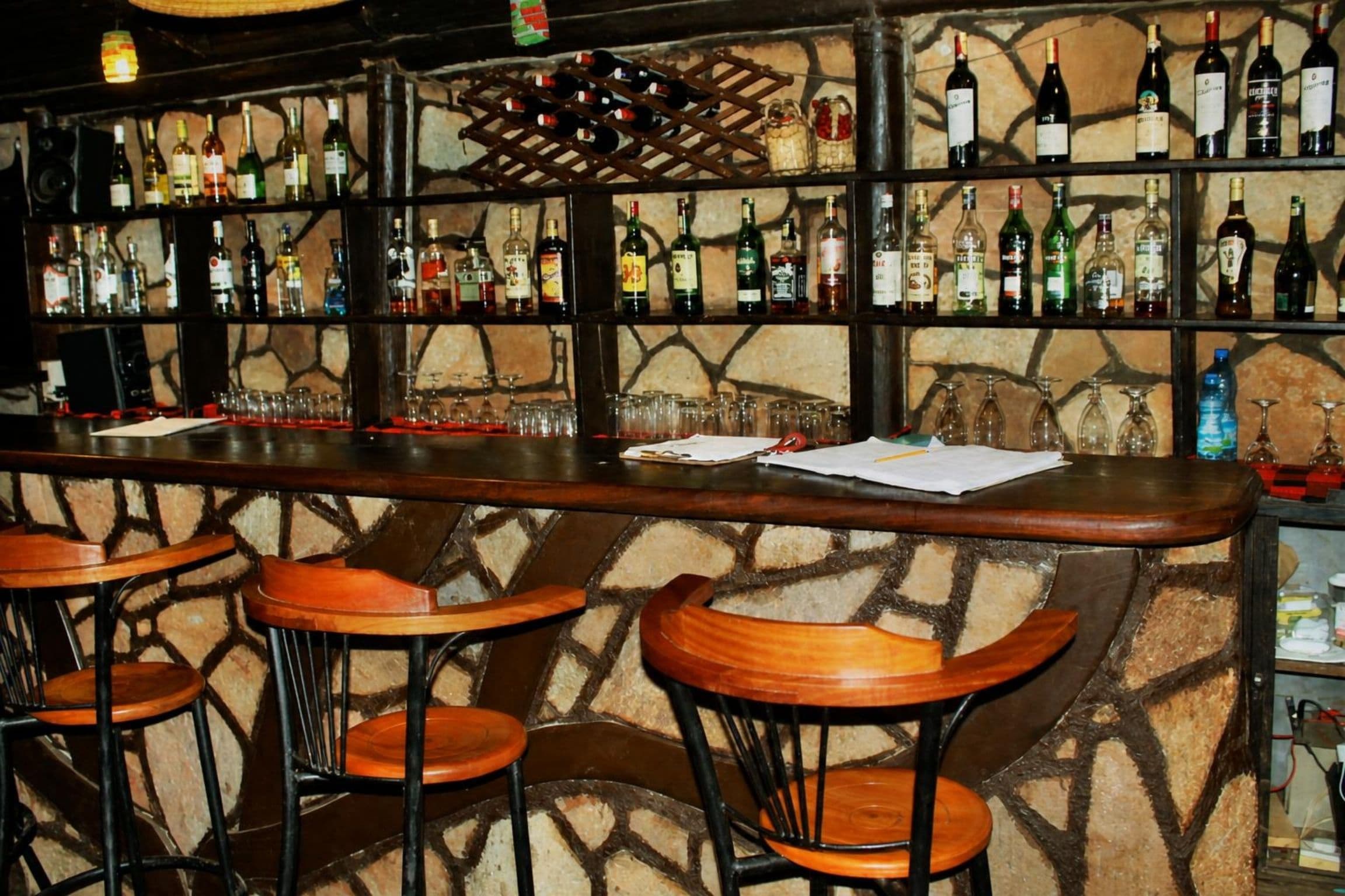 A bar area with multiple shelves of bottles, a counter, and bar stools.