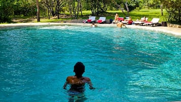 A swimming pool with clear blue water, surrounded by lounge chairs and a grassy area.
