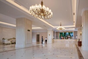 A spacious lobby with a polished marble floor, elegant chandeliers, and a reception area with a mural. - Vienna International Hotel (Sanya)