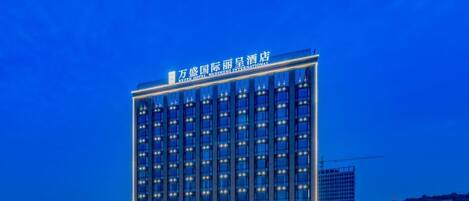 A multi-story hotel with a modern facade, illuminated windows, and a prominent signage at the top.