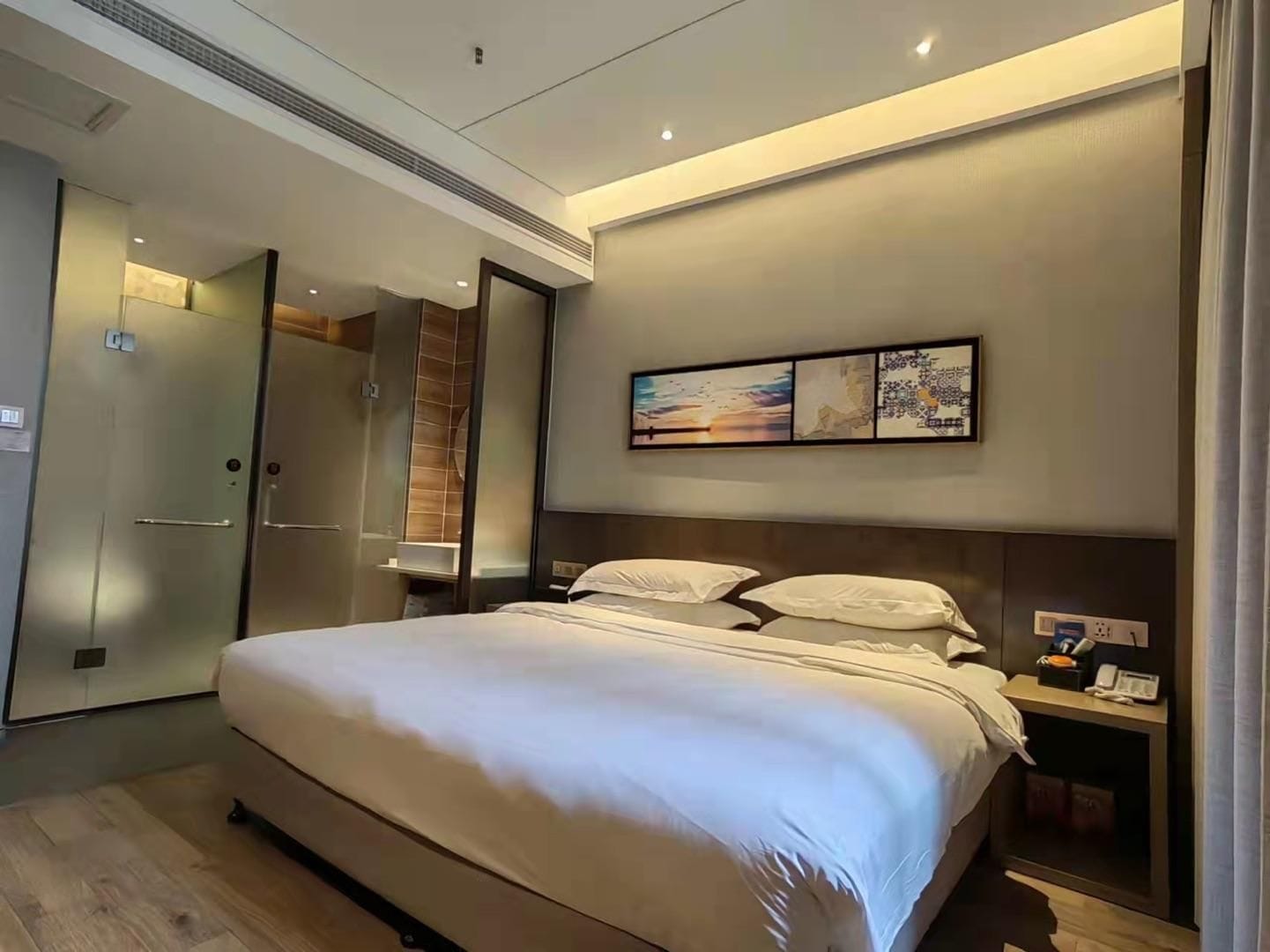 A modern hotel room with a large bed, a walk-in closet, and a shower area.