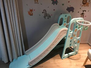 Un tobogán infantil con un adhesivo mural de animales y una ventana con cortinas.