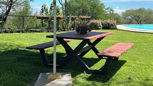 Uma mesa de piquenique com toldo, cercada por um gramado bem cuidado e uma piscina.