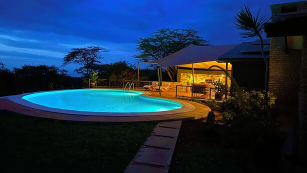Piscina com deck ao redor, área de estar coberta ao ar livre e um edifício com fachada de pedra.