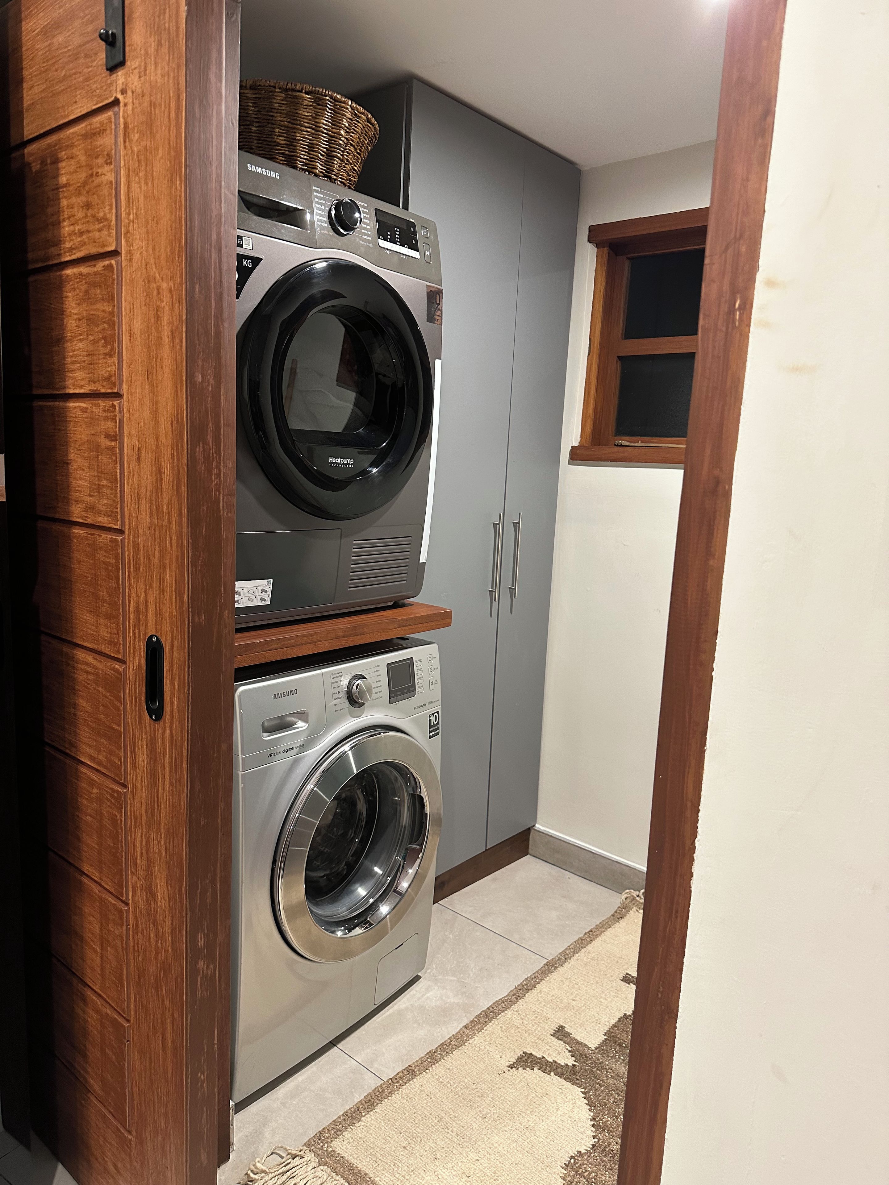 A laundry room with two stacked washers and dryers, wooden cabinets, and a window.