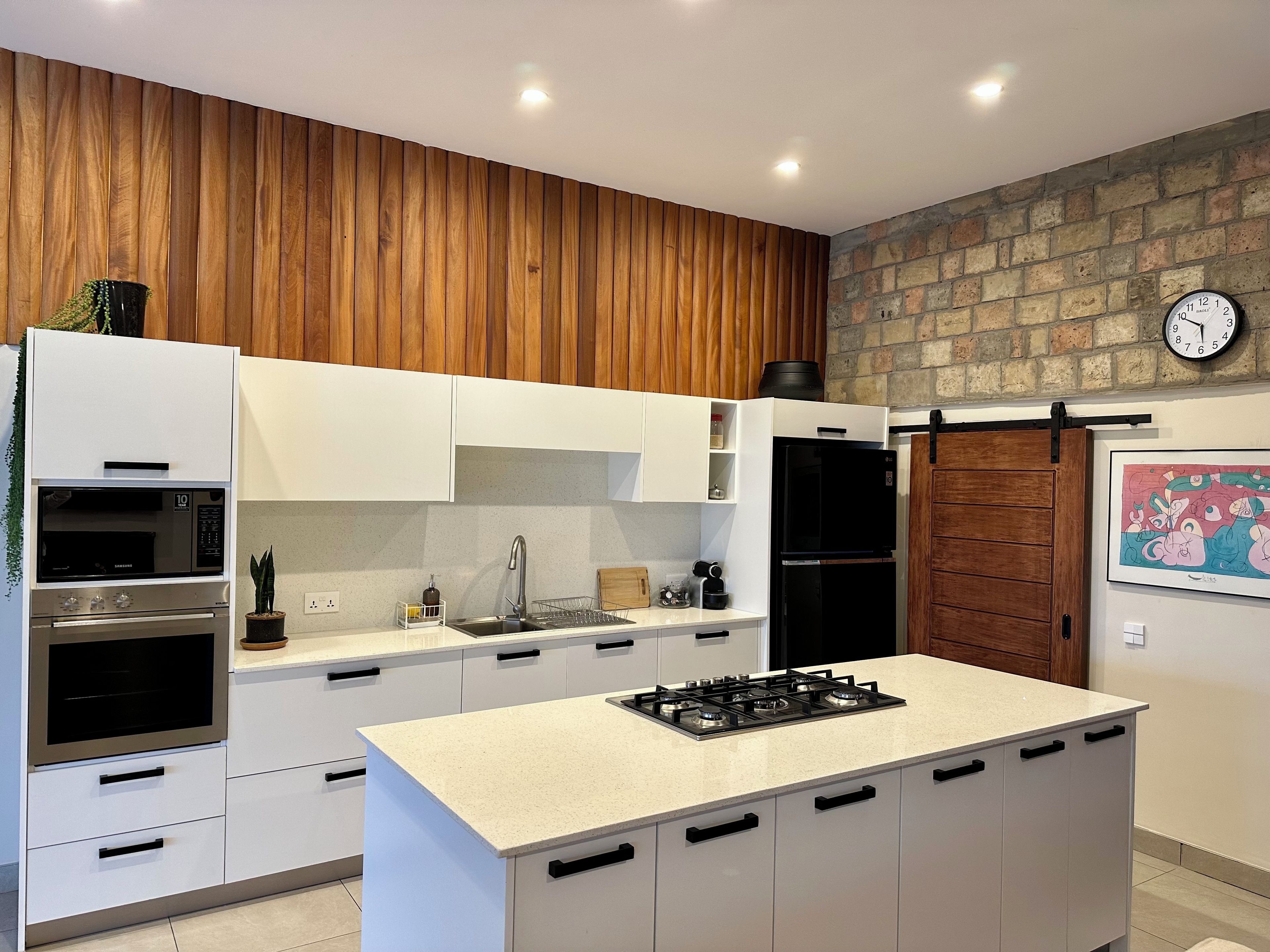 Una cocina moderna con armarios blancos, una isla central con estufa y una pared de ladrillo.