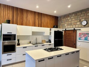 A modern kitchen with white cabinetry, a central island with a stove, and a brick wall.