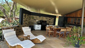 Um pátio externo com área de estar coberta, churrasqueira e mesa de jantar.