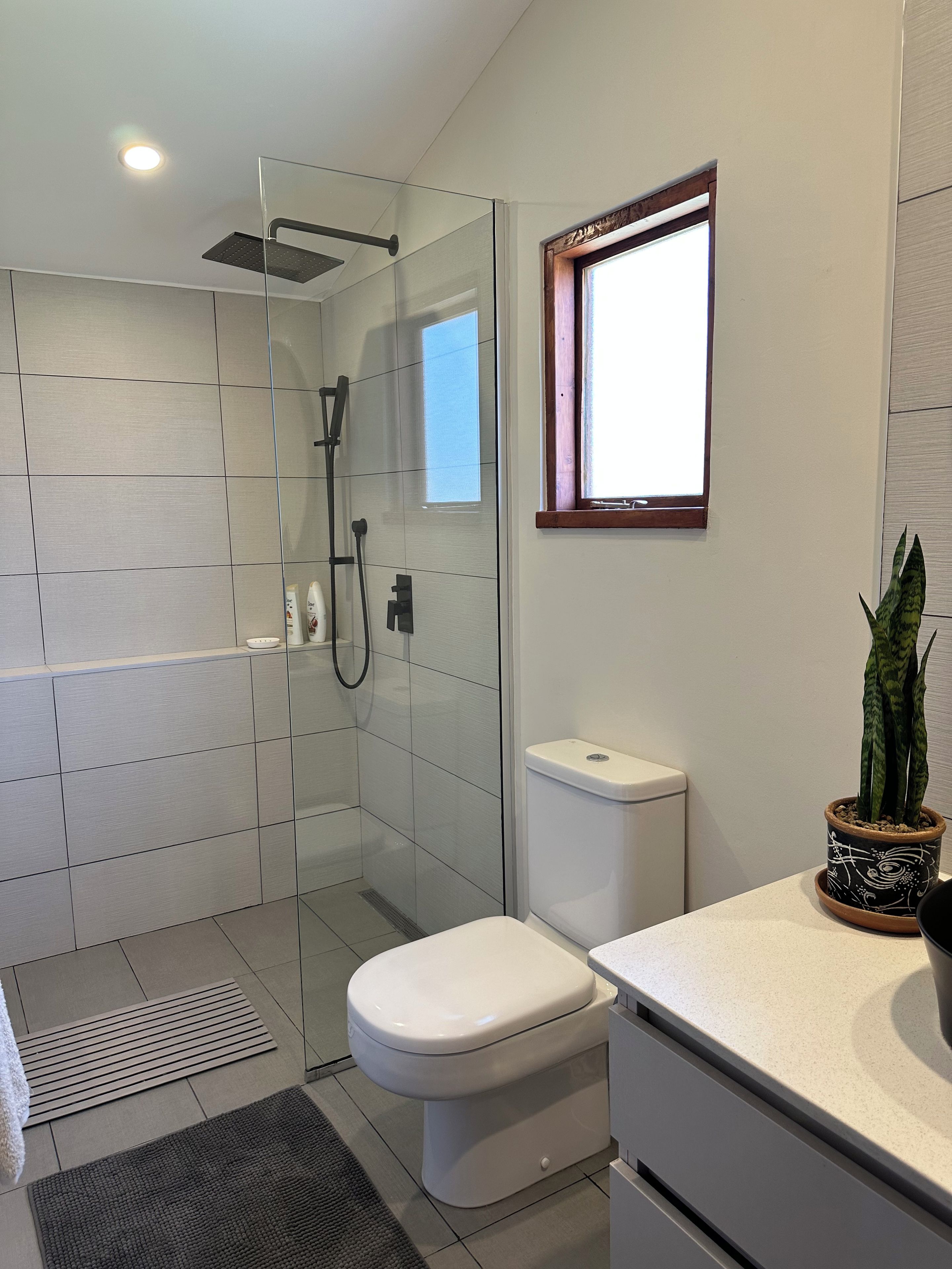Un baño moderno con cabina de ducha de vidrio, inodoro, lavamanos y ventana que proporciona luz natural.