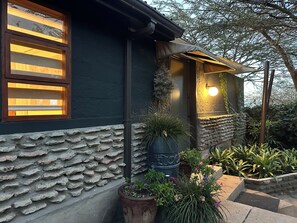Una casa con fachada de piedra, una ventana con persianas y una planta en maceta en primer plano.