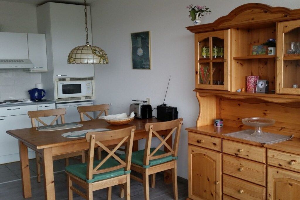 Une cuisine avec une table en bois, des chaises, un four à micro-ondes, un grille-pain et un meuble contenant de la vaisselle en verre.