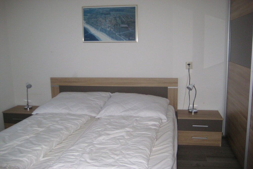 Ein Schlafzimmer mit einem Bett, zwei Nachttischen, einer Wandlampe und einem Nachtschränkchen.