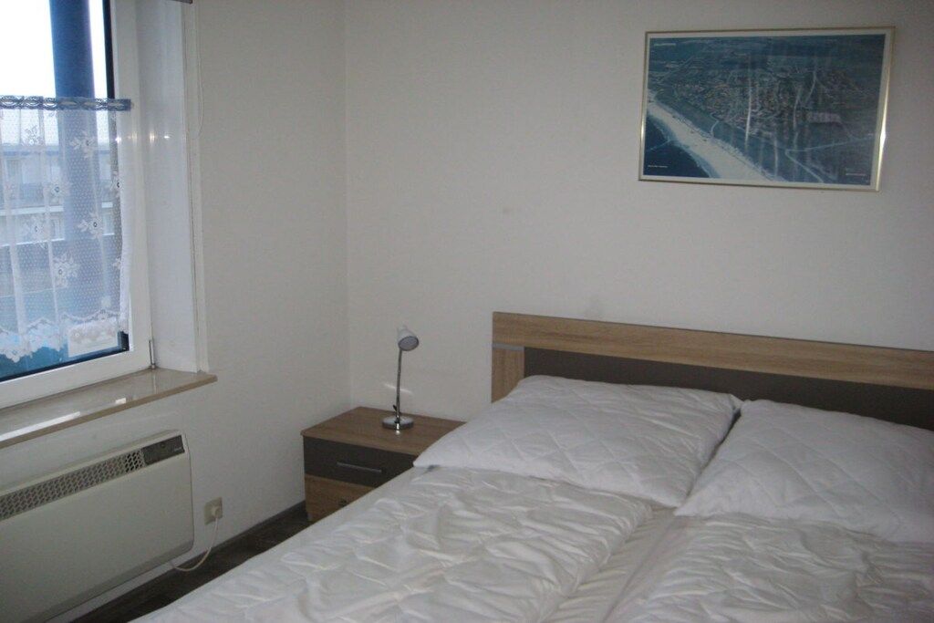 Un dormitorio con cama, mesita de noche, lámpara, ventana con vistas y un cuadro colgado en la pared.