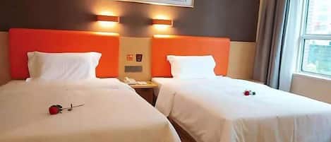 A hotel room with two beds, a framed artwork above the beds, and a window with curtains.