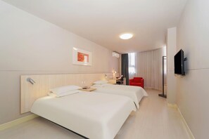 Quarto de hotel com duas camas, uma escrivaninha, uma cadeira, uma TV e um quadro na parede.