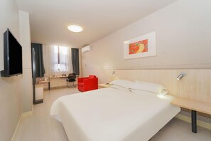 Quarto de hotel com cama, escrivaninha, cadeira, televisão e um quadro na parede.